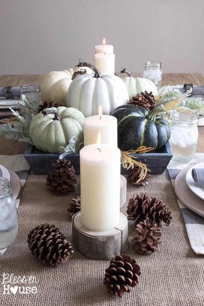 Thanksgiving table centerpieces with green and blue pumpkins and pinecones along a jute runner