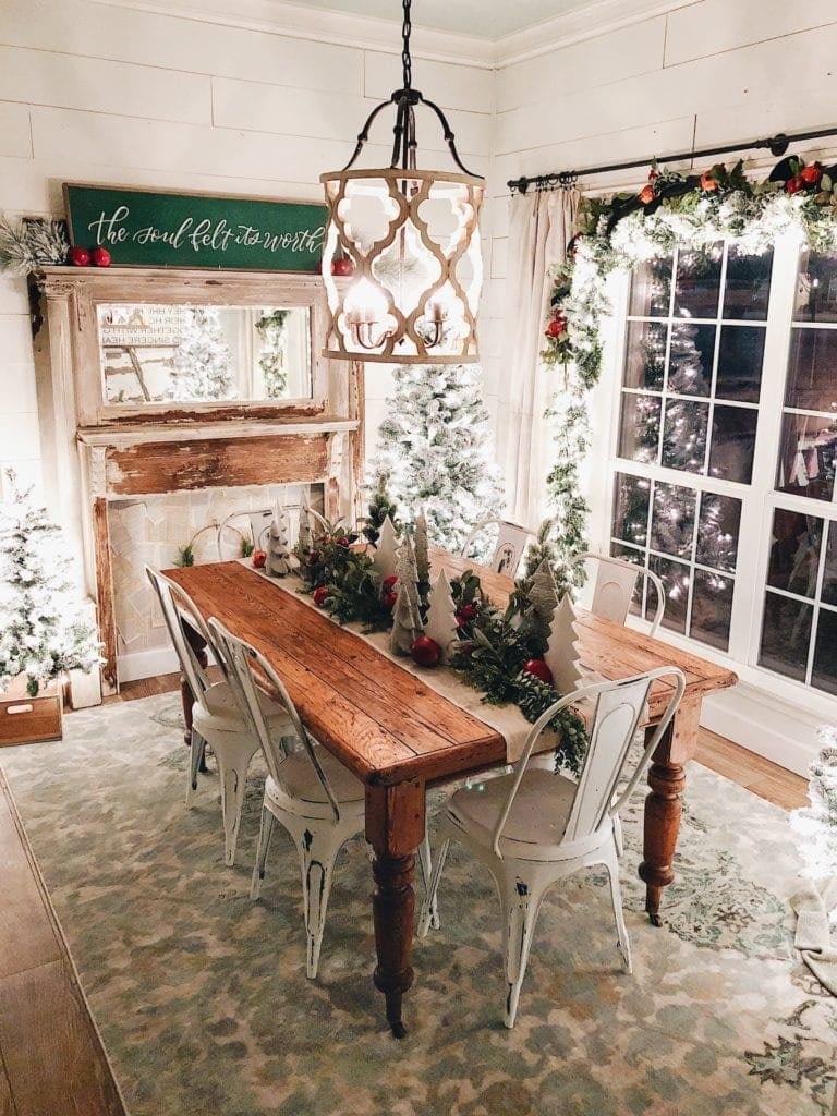 Chrismtas dining room lit up with twinkle lights and a table runner made from garland and mini wood trees