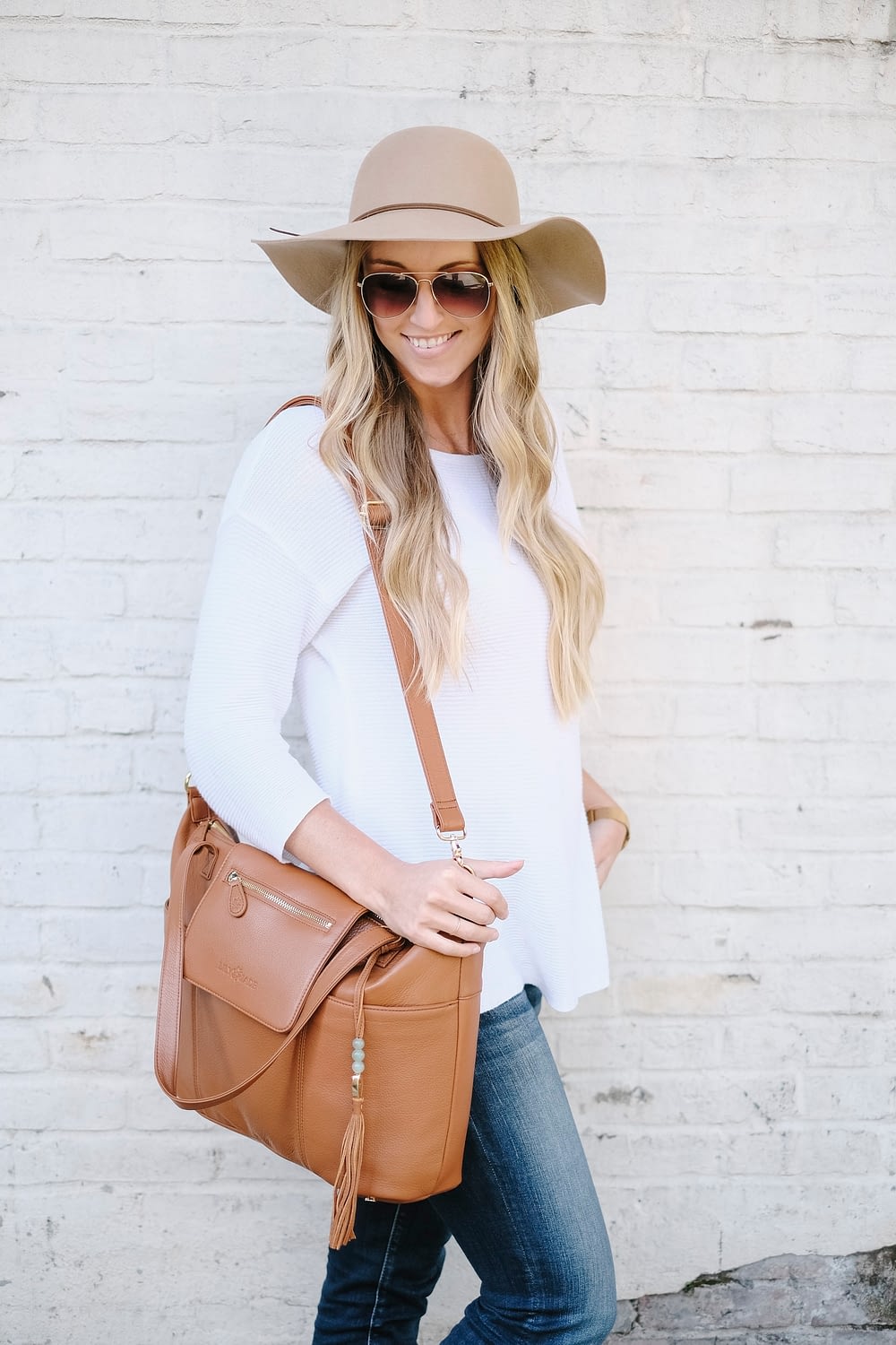 blonde woman carrying leather diaper bag with messenger strap on shoulder
