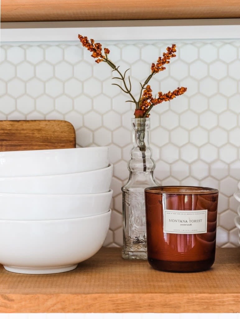 a kitchen shelf decorated for fall with a Montana forest candle