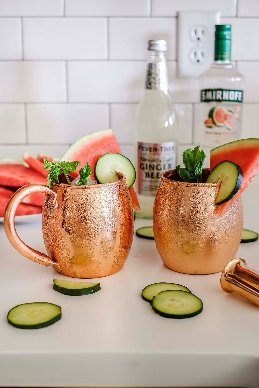 Two copper mugs with ingredients to make cucumber watermelon moscow mules