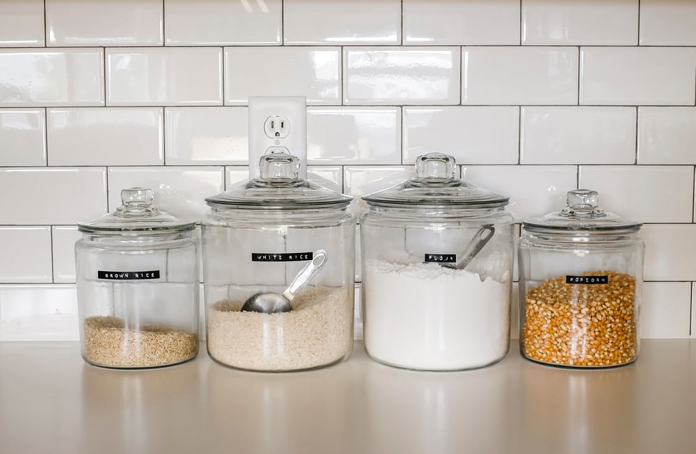 rice, flour, and popcorn jars on a white counter top with a white subway tile back splash