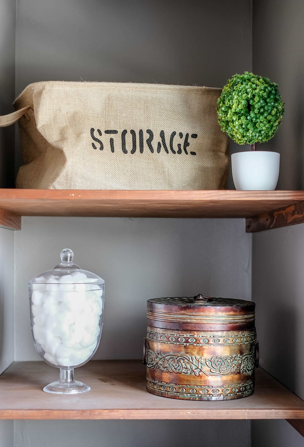 bathroom linens shelves styled with burlap, greenery, and a glass jar for cotton balls