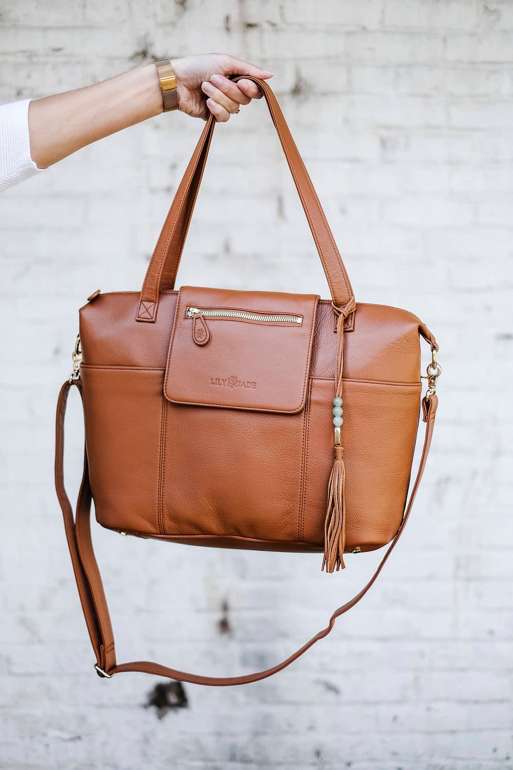leather diaper bag with multiple straps held in front of white wall