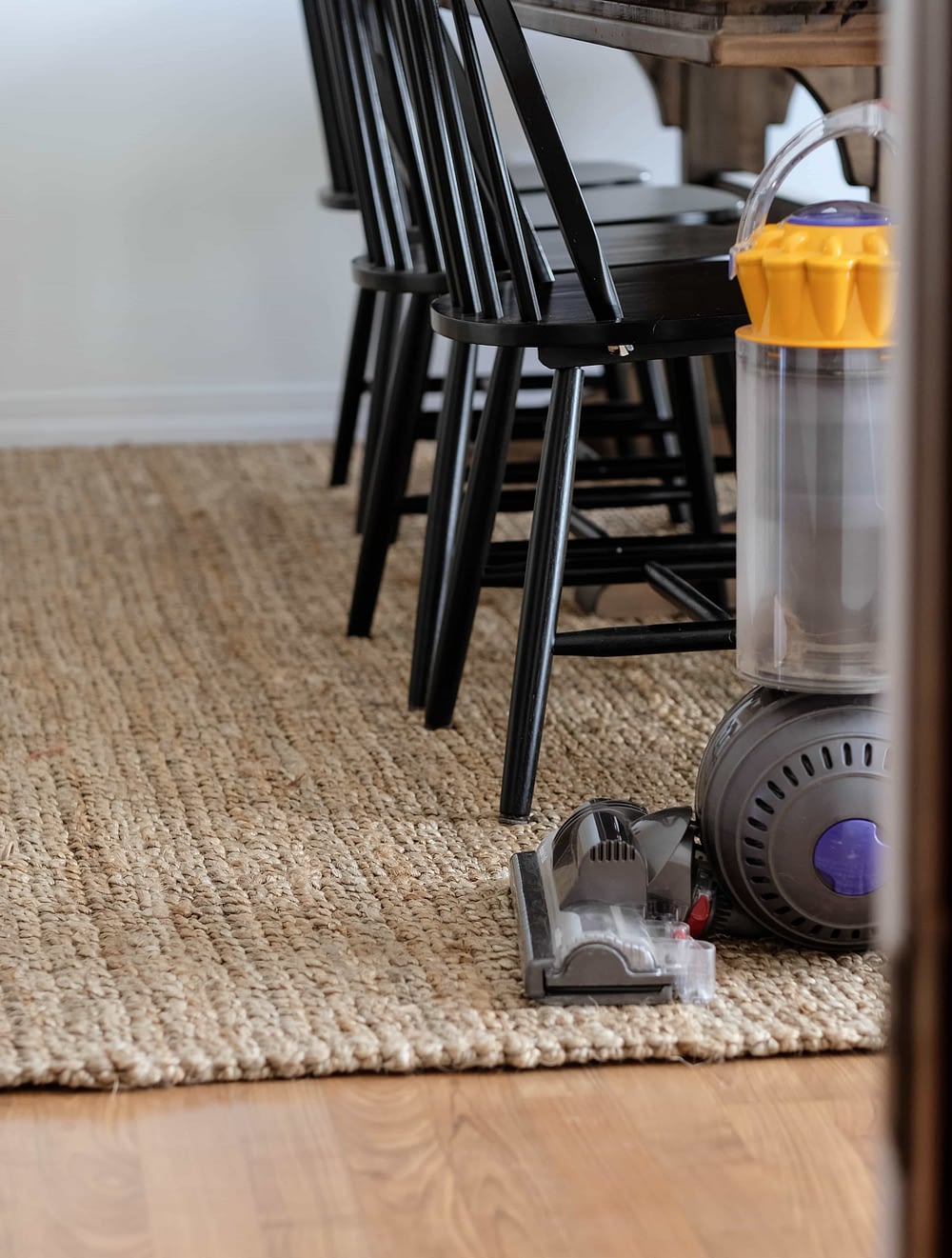 Jute rug in dining room with table and chairs. Dyson vacuum in foreground.
