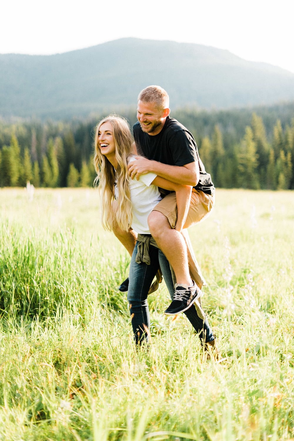 Blonde girl giving husband a piggy back ride in the mountains while both laugh