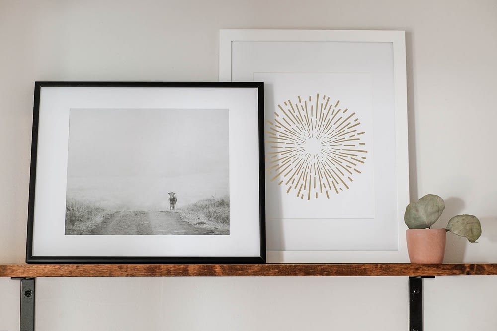 bathroom shelf styled with a framed black and white cow print, and a decorative firework print