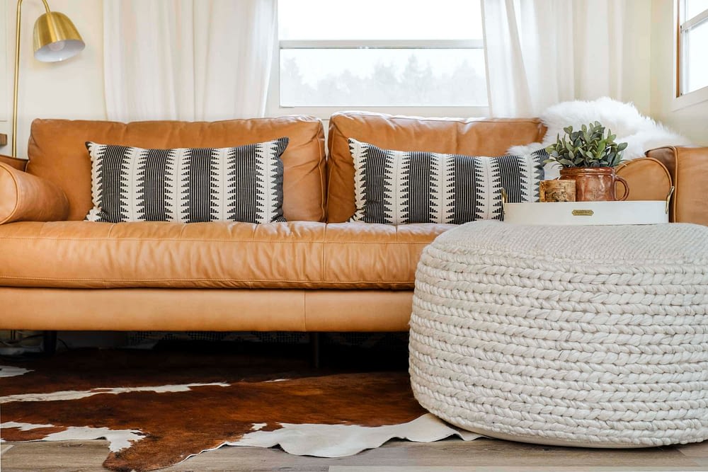 a large fabric floor pouf in front of a leather sofa with a tray on top