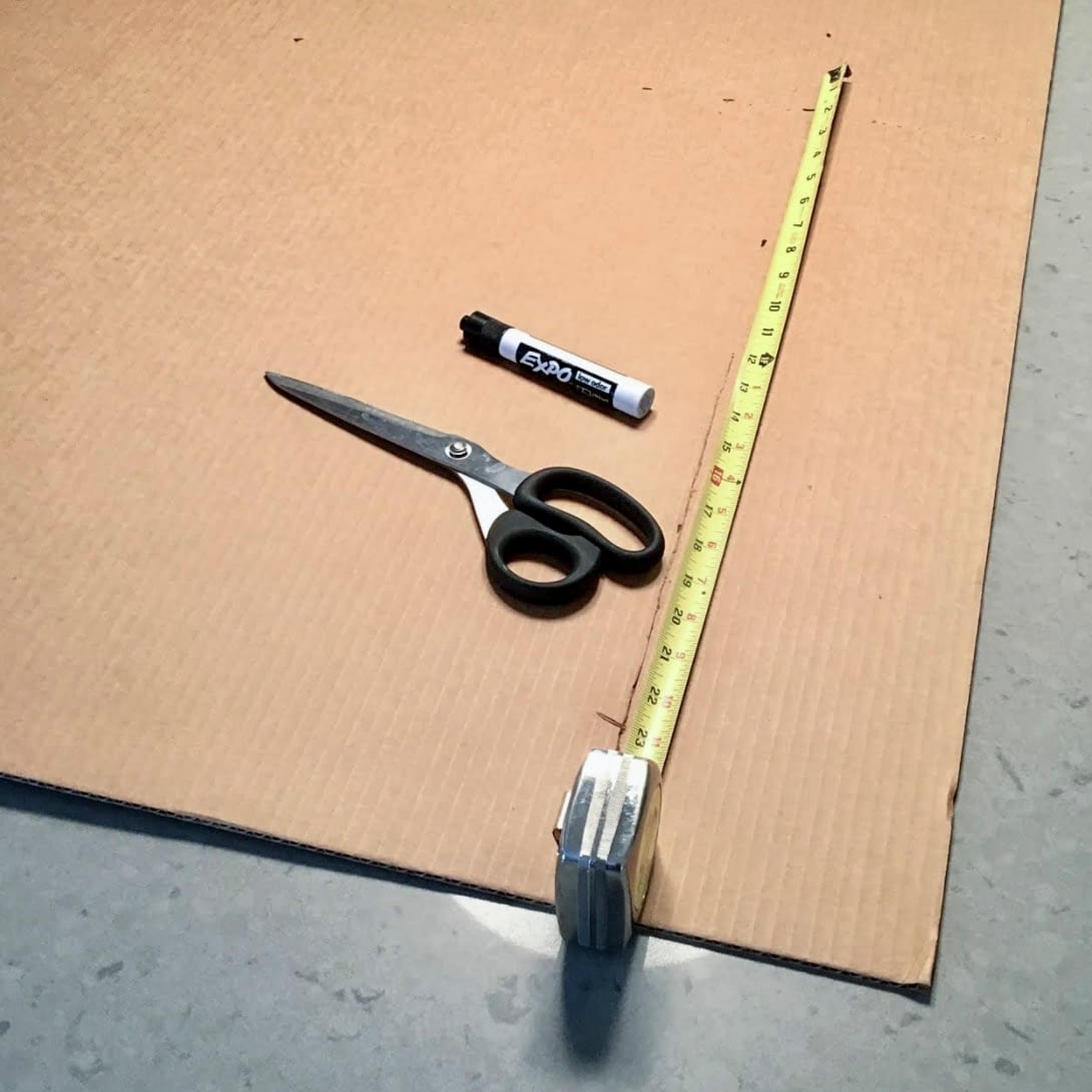 Flat cardboard with tape measure, scissors, and expo marker laying on top