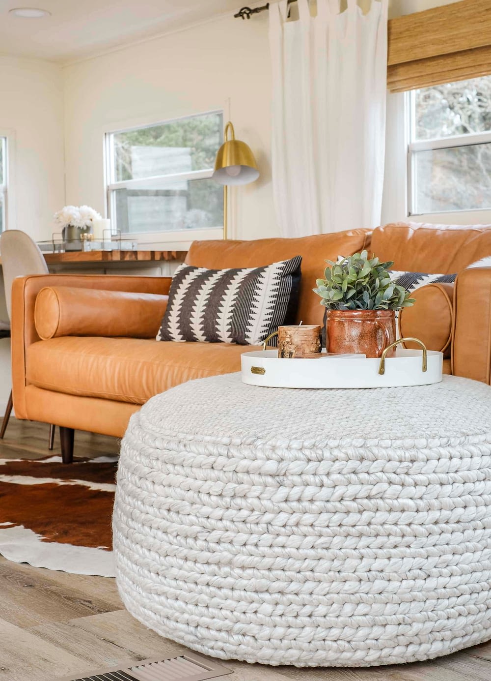 Large pouf with a tray on top in front of brown leather sofa