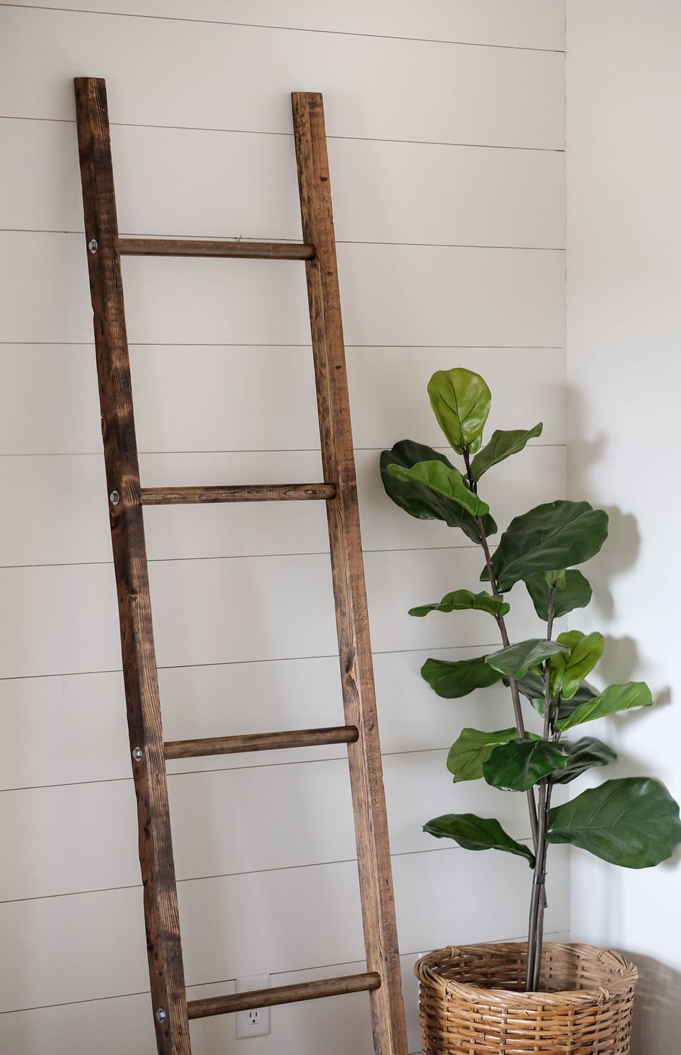 A walnut stained blanket ladder leaning against a white shiplap wall.