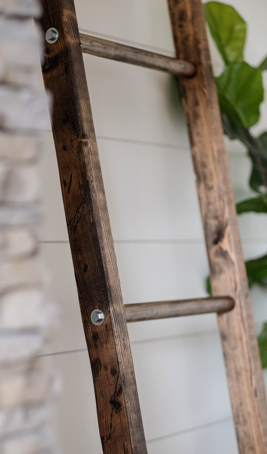 A walnut stained blanket ladder leaning against a white shiplap wall