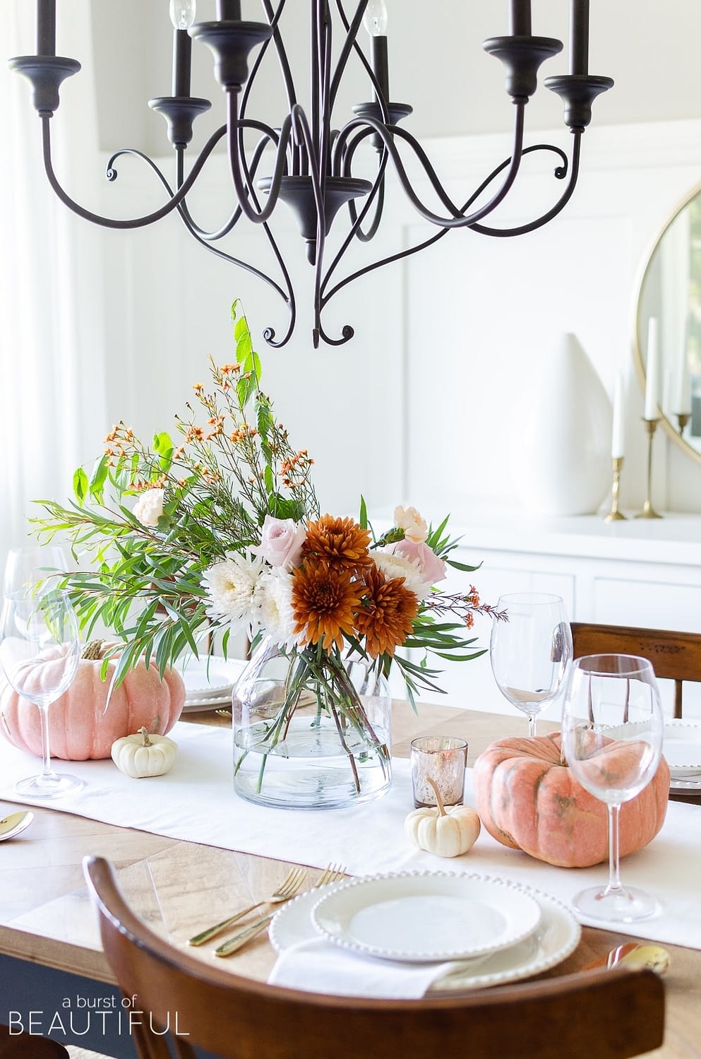 Thanksgiving table centerpieces with a fall floral arrangement and orange pumpkins