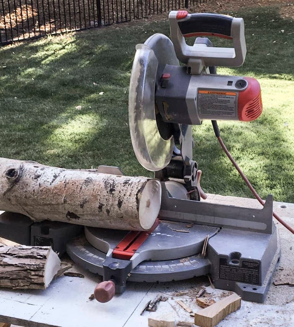 A miter saw sitting on a table outside cutting logs into small round pieces
