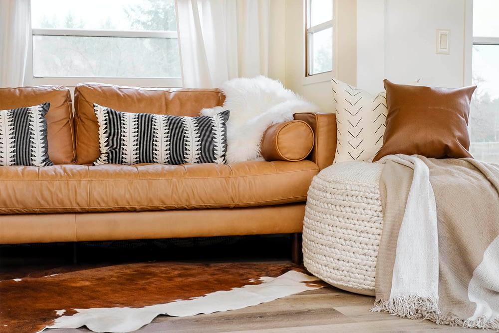 Large woven pouf in front of a leather sofa with pillows and a blanket