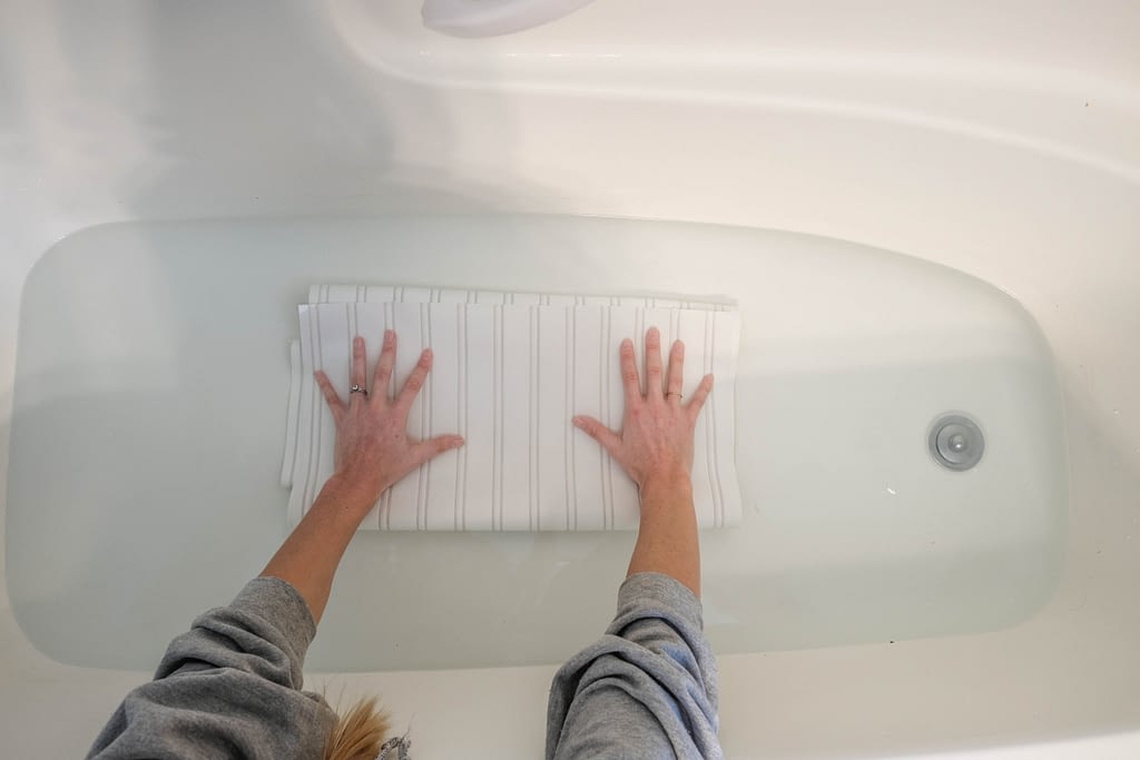 Overhead view of someone soaking beadboard wallpaper in bathtub