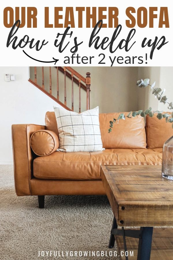 Leather sofa with white throw pillow and text overlay that reads "Our leather sofa, how its held up after 2 years!"