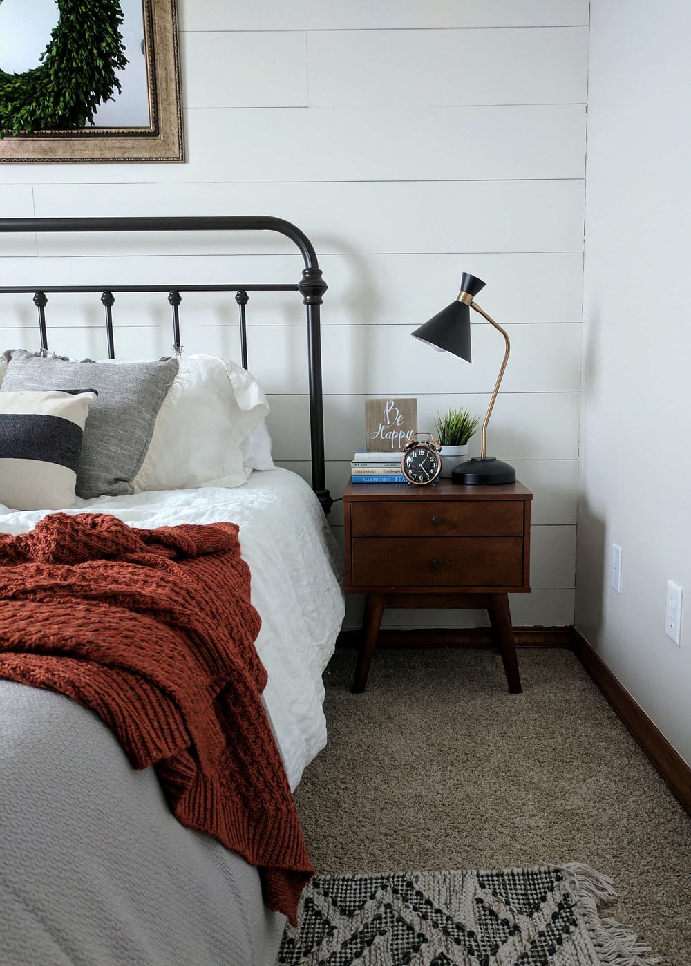 a nightstand styled with books, alarm clock, and a lamp in a farmhouse bedroom