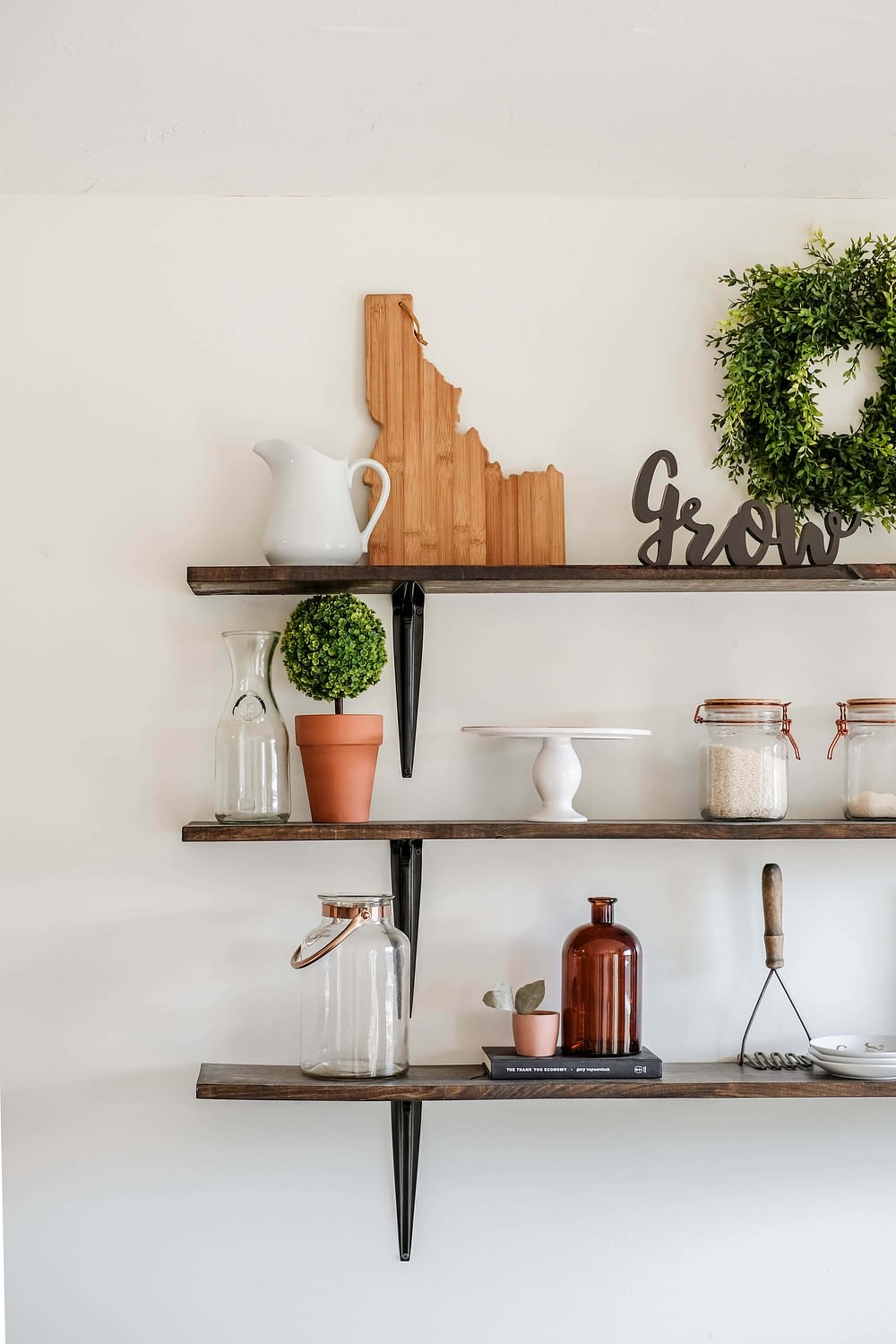 dining room shelves styled with a cutting board, a cake stand, potted greenery and glass canisters 
