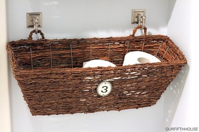 Wicker basket with bathroom items in it hanging from two hooks on the wall