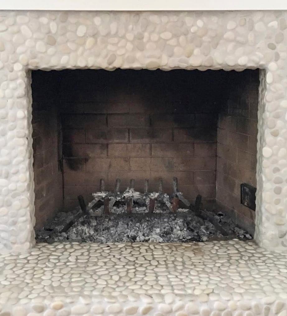 Empty fireplace opening with ashes inside and small pebble rocks surrounding it