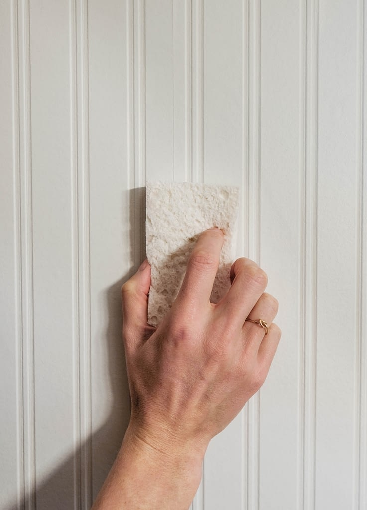 Closeup of a hand holding a sponge against beadboard wallpaper