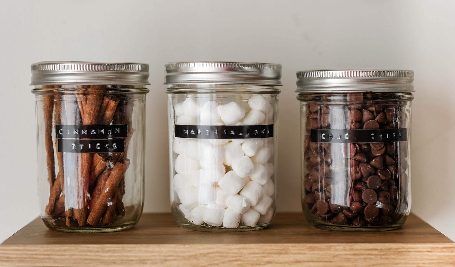 mason jars with embossed labels cinnamon sticks, marshmallows, and chocolate chips. 