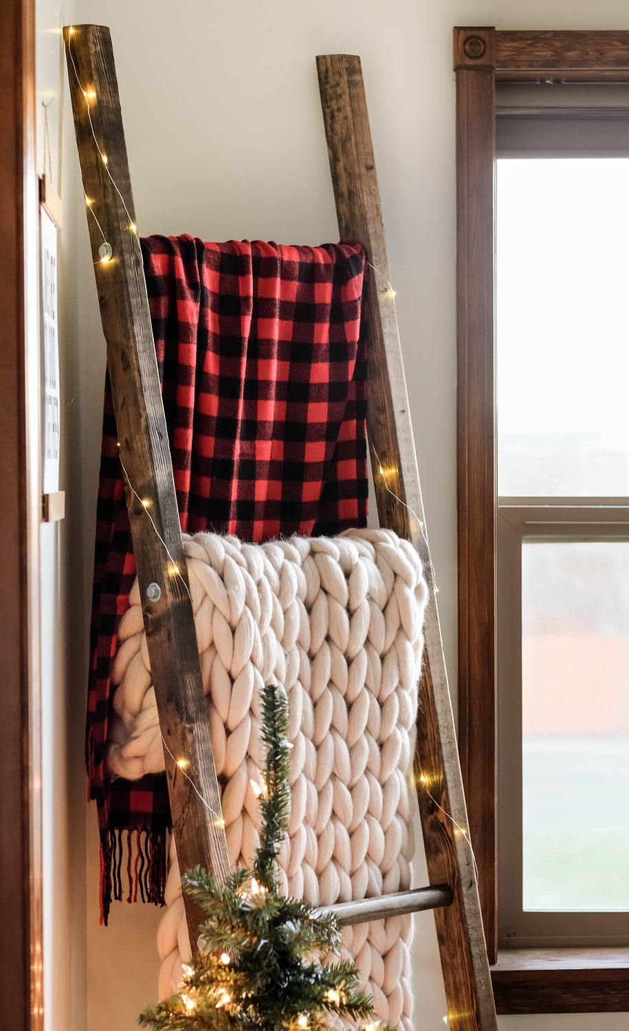 a blanket ladder holding blankets with christmas lights strung on it