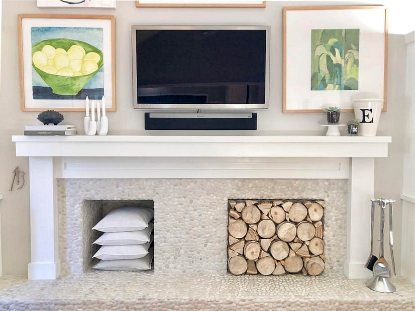 Fireplace mantle with art and TV hung above it and stacked logs in the fireplace opening
