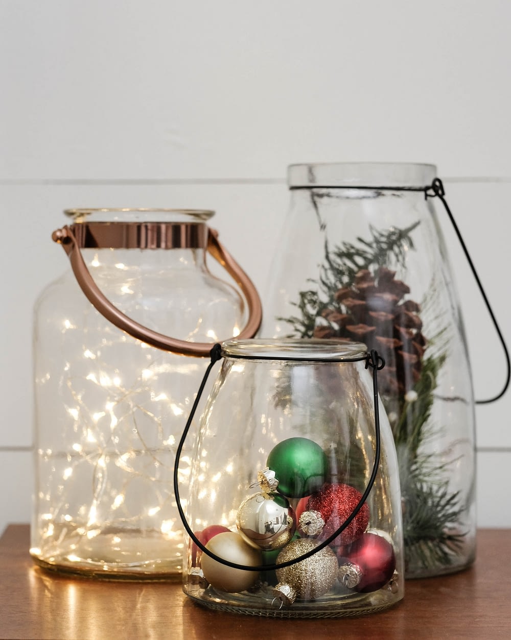 Christmas decor using 3 glass lanterns filled with twinkle lights, Christmas ornaments and pinecones
