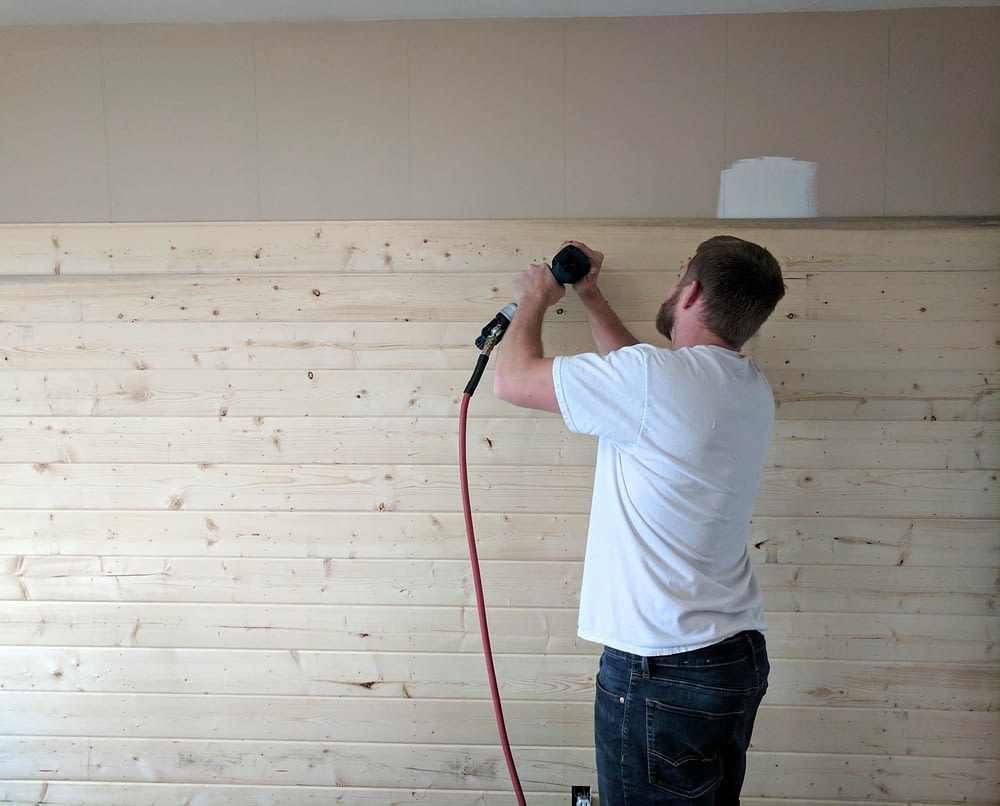 A man using a nail gun on a DIY wood accent wall