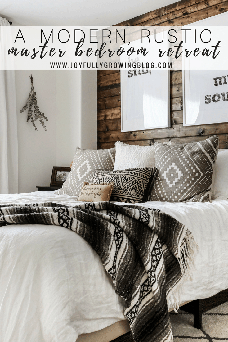 A rustic bedroom with a closeup of the bedding including throw pillows and blanket, up against a wood plank wall. Text overlay "A Modern, Rustic Master Bedroom Retreat - www.joyfullygrowingblog.com"