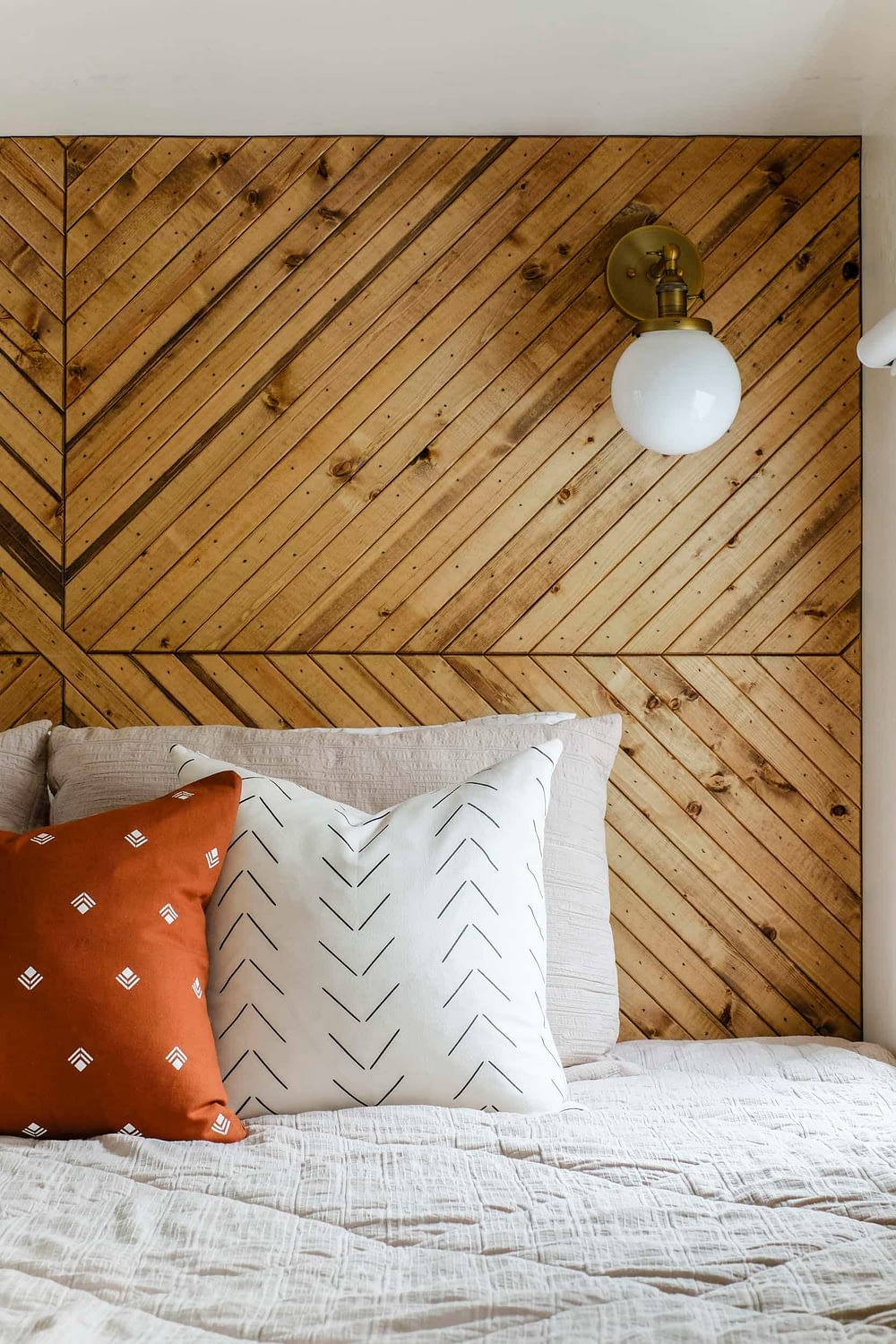 Closeup of wood plank accent wall behind bed and a brass wall sconce