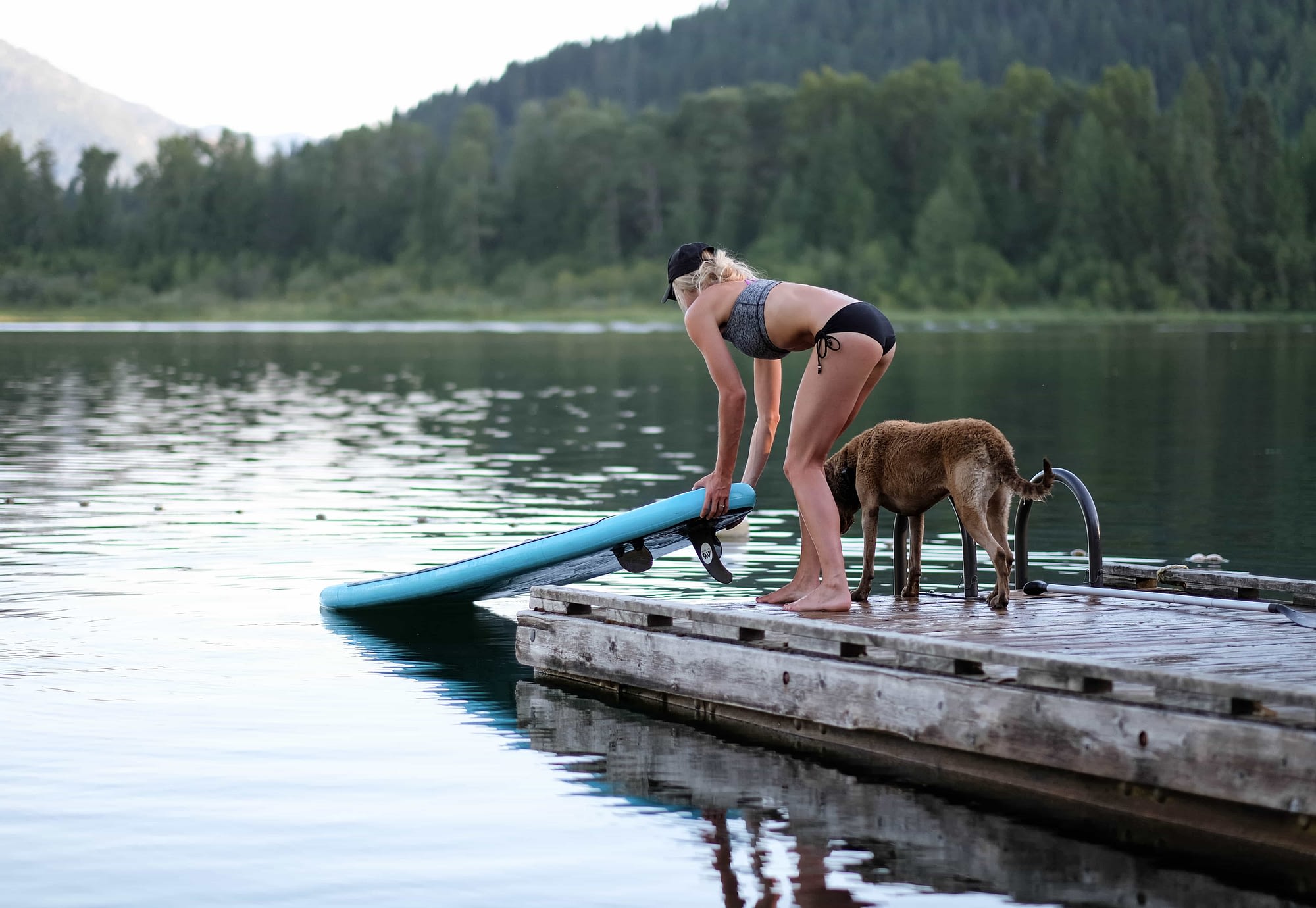 woman and dog standing on dock launching a paddle board into the lake