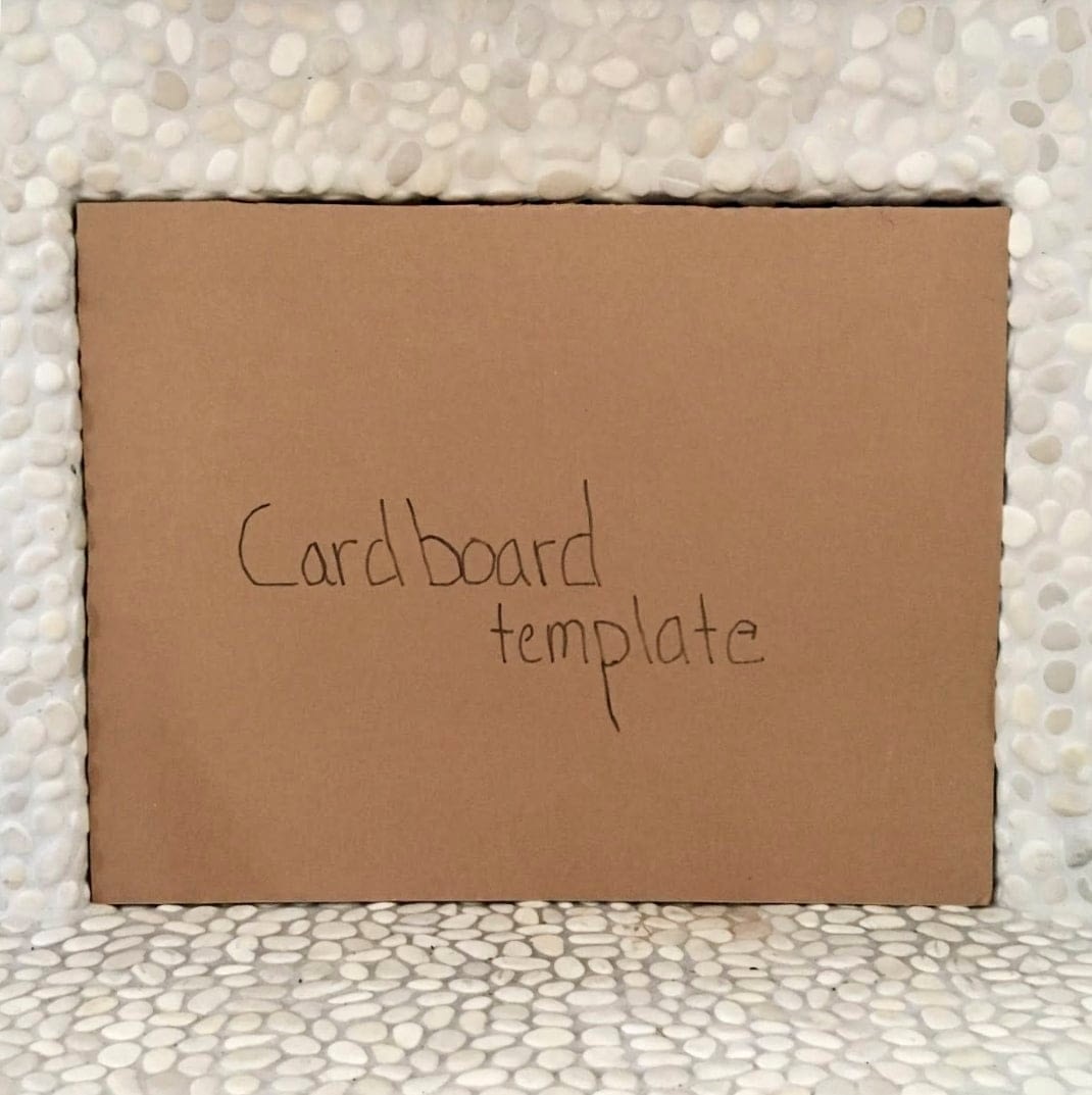Square cardboard cutout inside of a fireplace opening with the words 'Cardboard template' written on it