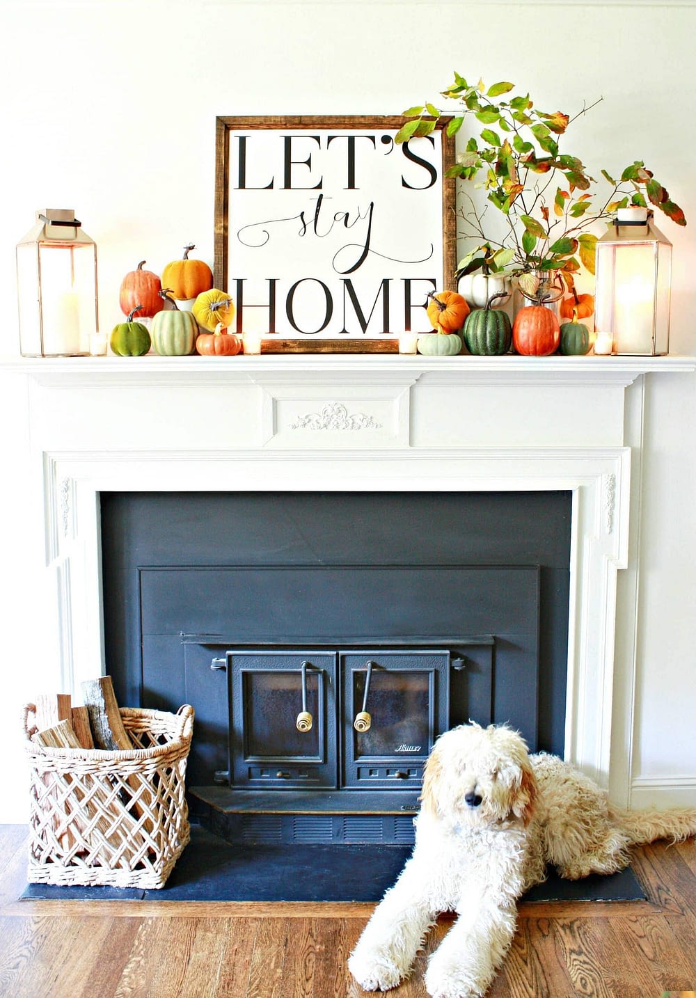 Fall mantel decor with a print that reads Let's Stay Home surrounded by mini pumpkins and candles
