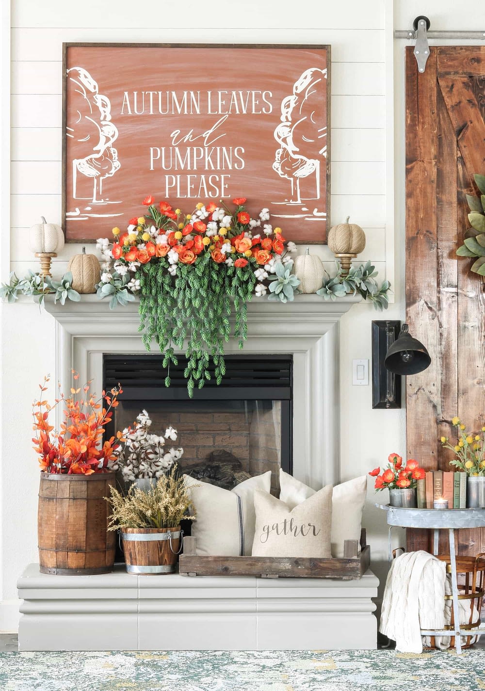 Fall mantel ideas using orange florals, wooden barrels, and cozy pillows centered under a giant piece of artwork