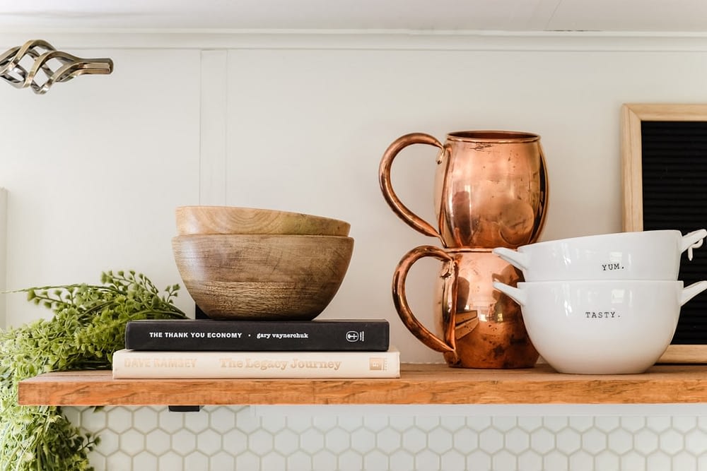 open shelving decorated with books, greenery, wood bowls and copper mugs