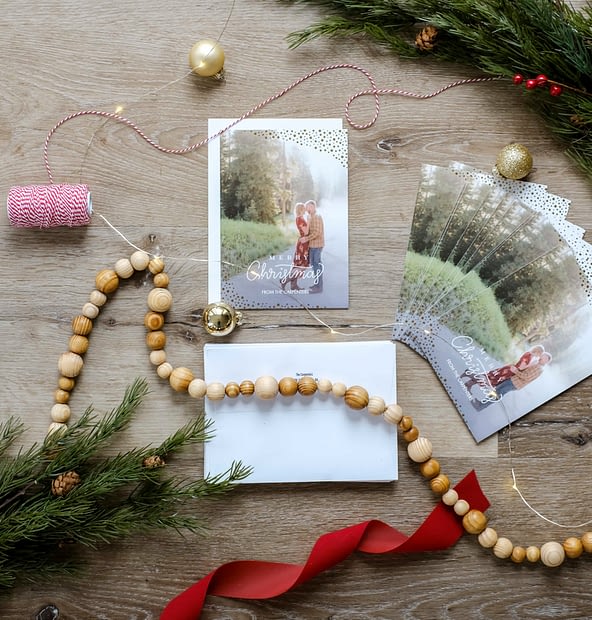 Overhead view of a personalized Christmas card layed out with ribbon, garland, and greenery