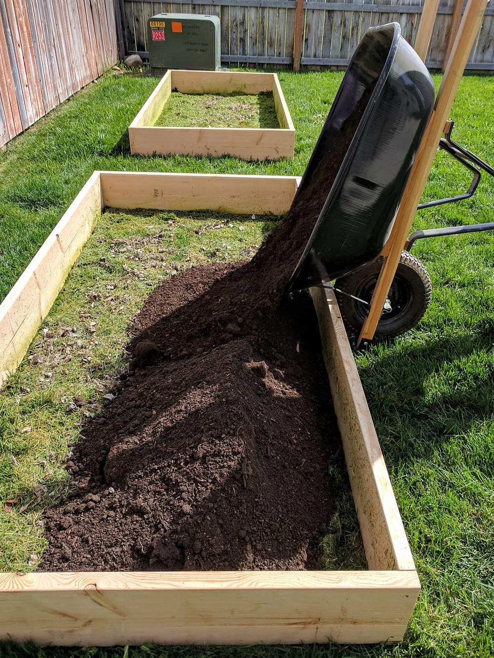 A wheel barrow dumping soil into a raised garden bed