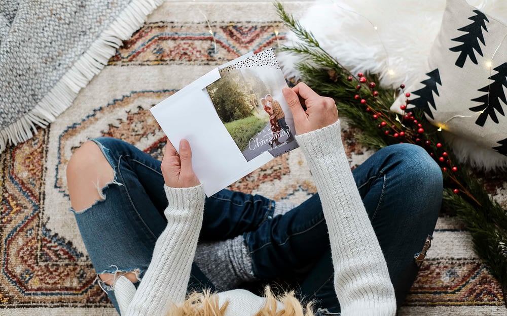 A woman sitting on the floor putting a personalized Christmas card into an envelope