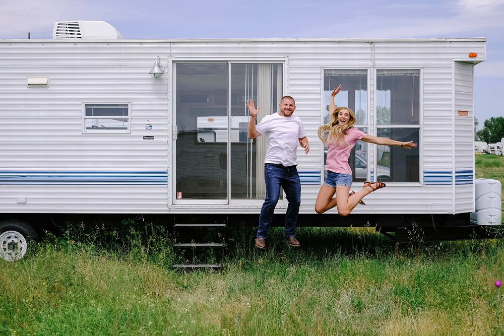 A couple embracing RV life jumping for joy in front of their 2005 park model trailer