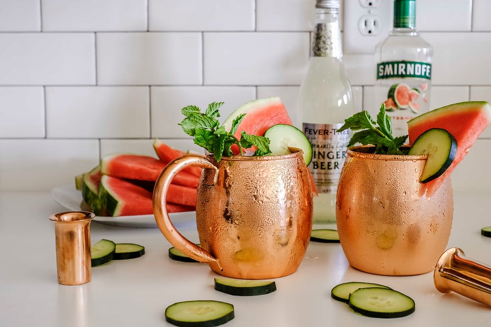 Two copper mugs with cucumber watermelon moscow mule ingredients