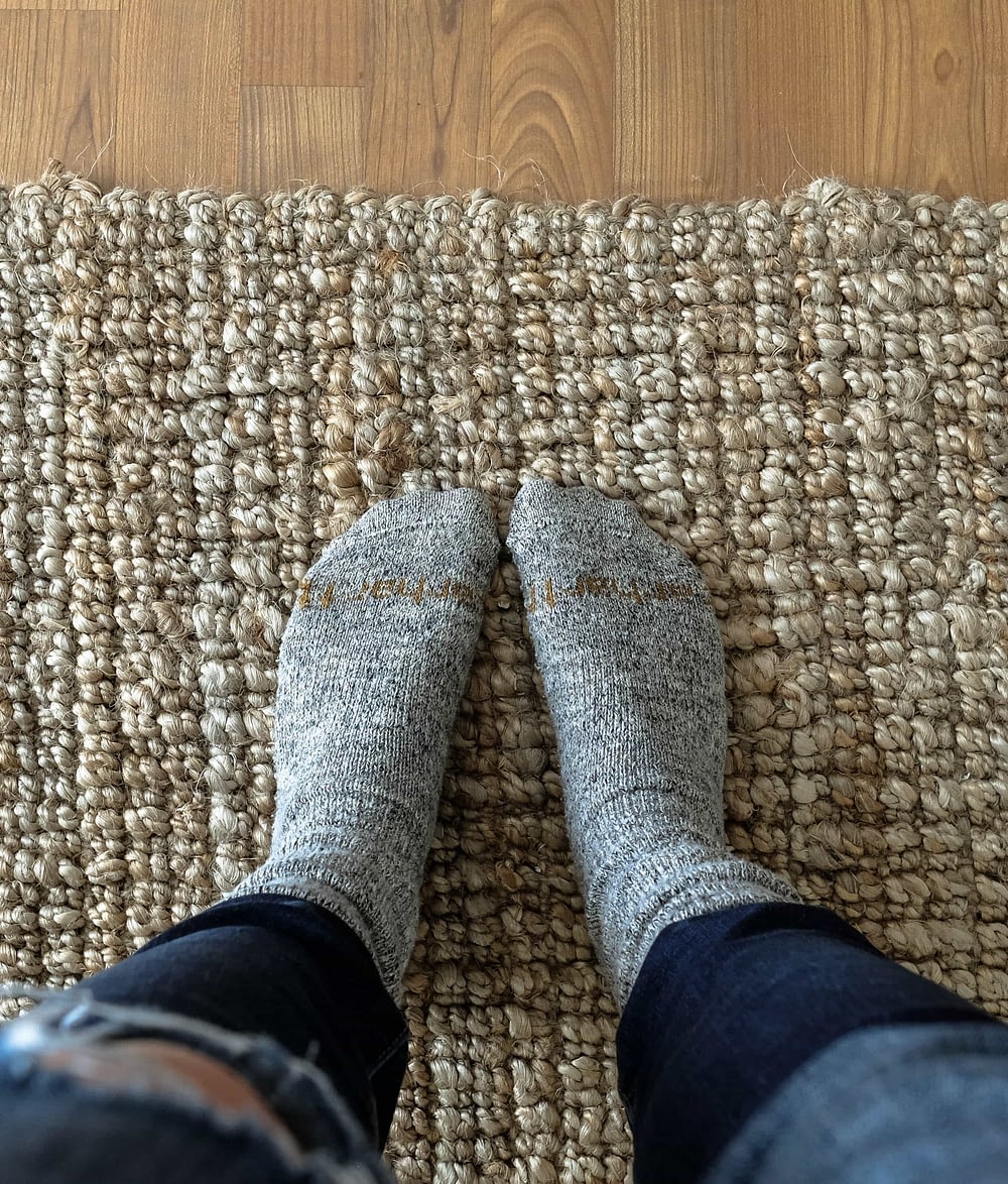 Close up of feet wearing wool socks standing on a jute rug