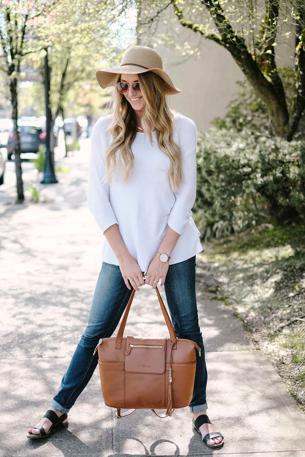 diaper bag review featuring a blonde woman holding leather bag on sidewalk
