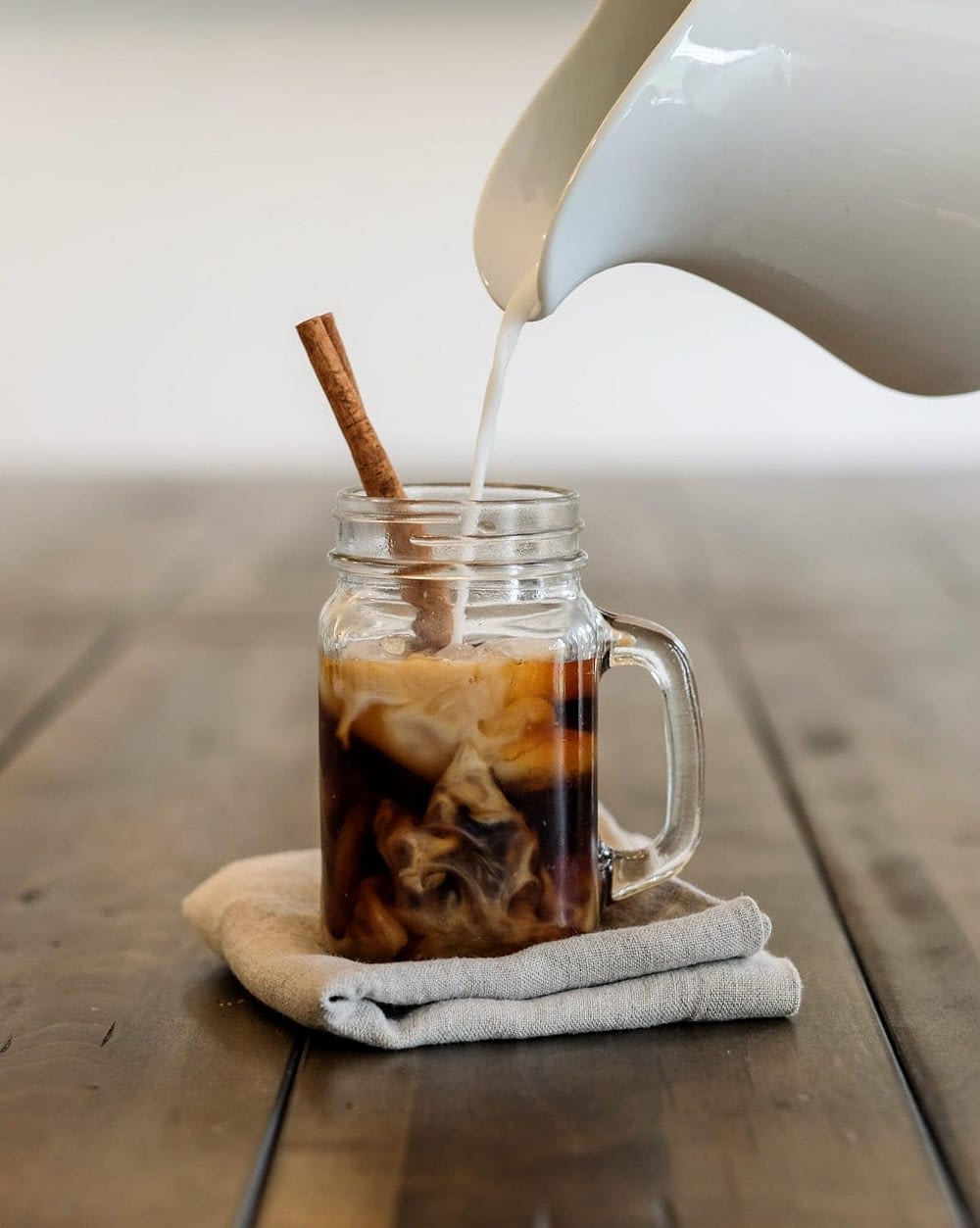 Cream being poured into a cold brew coffee in a mason jar