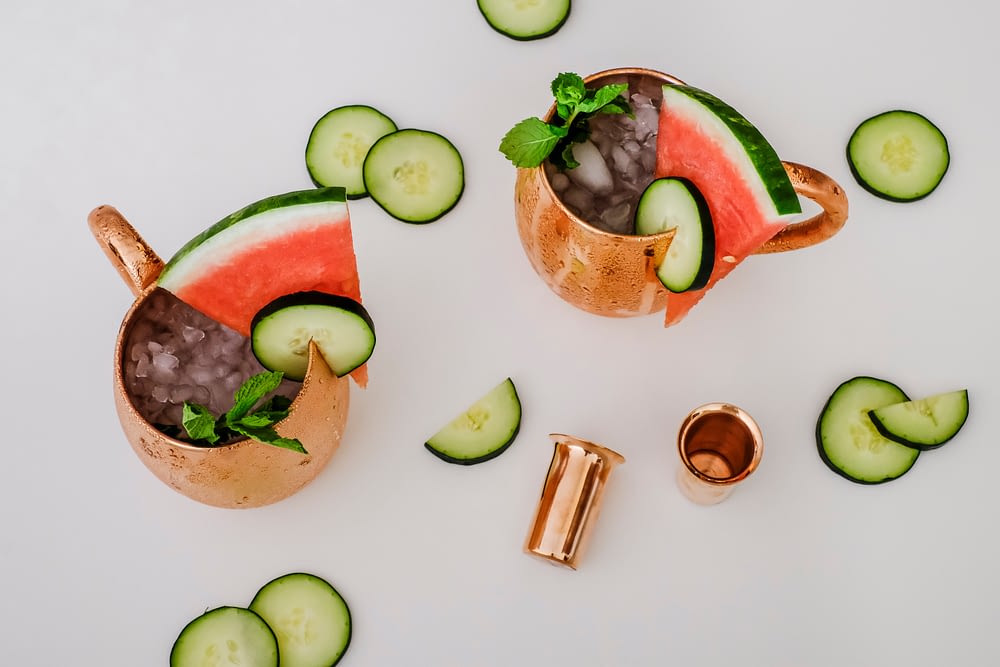 View looking down on two copper mugs filled with cucumber watermelon moscow mule ingredients 