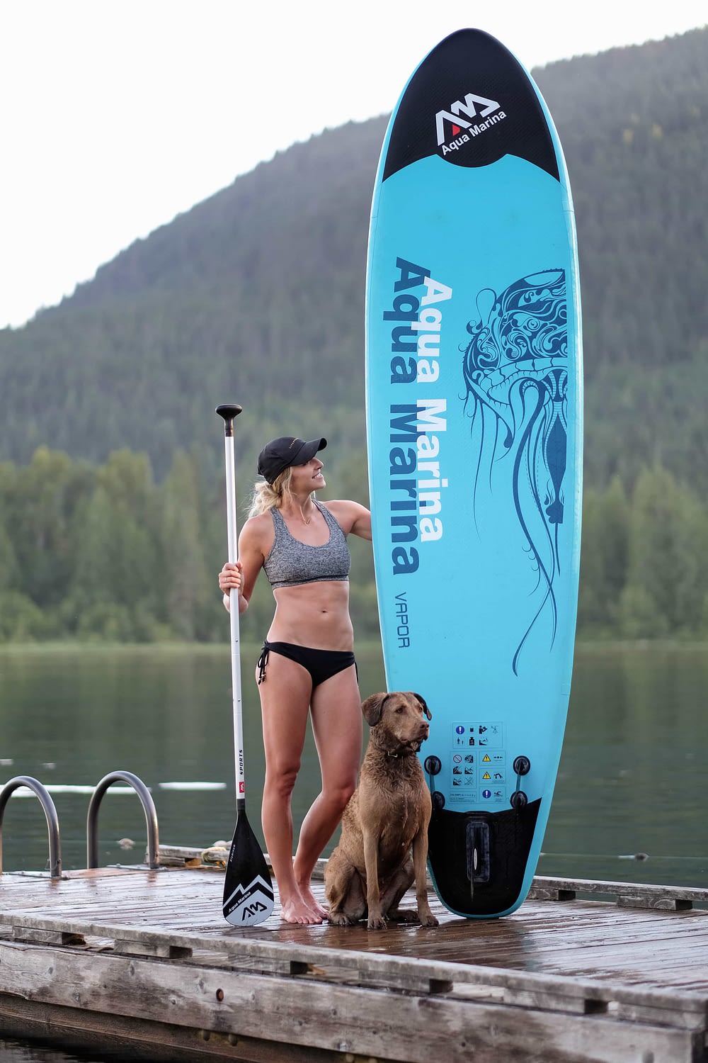 girl holding her inflatable sup on a dock with a dog
