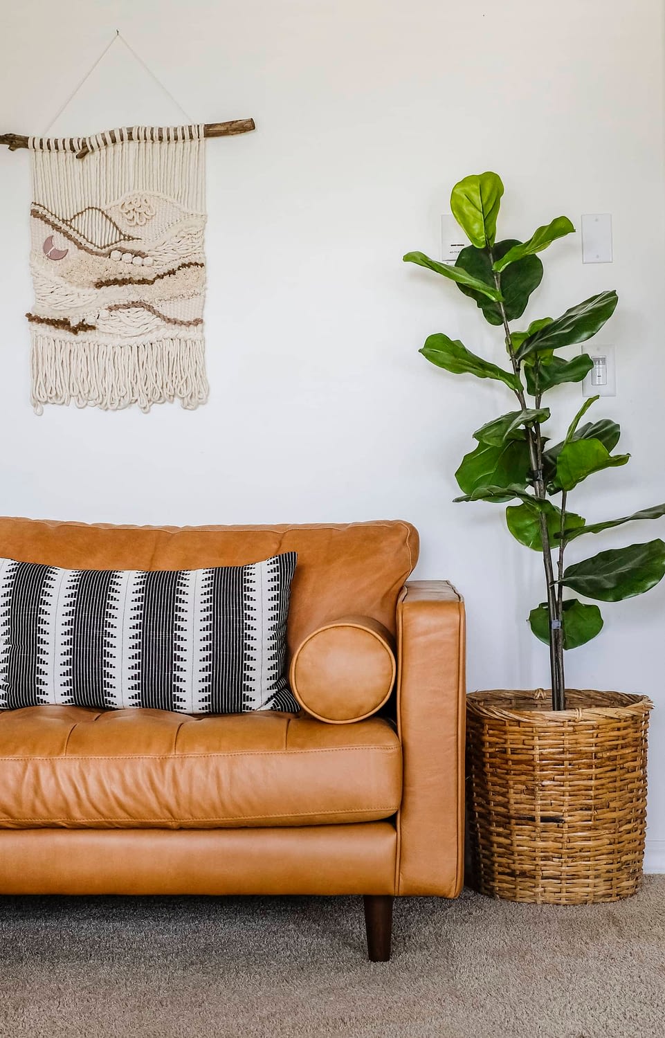 Leather sofa with black throw pillow next to an artificial fiddle leaf fig tree