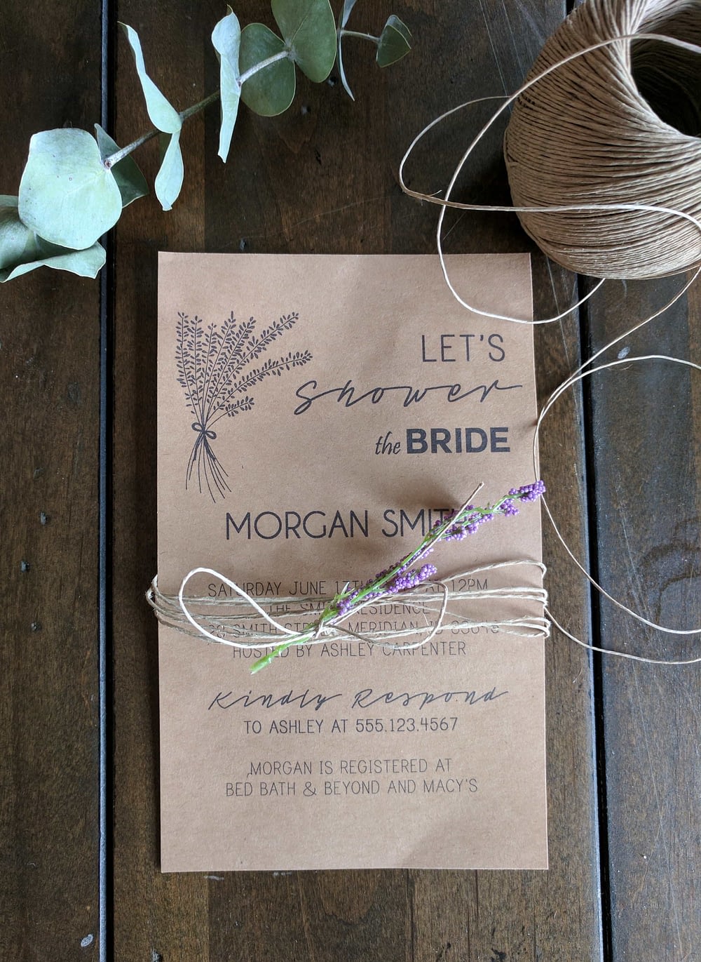 A DIY wedding Invitation sitting on a wood table wrapped in twine with lavender 